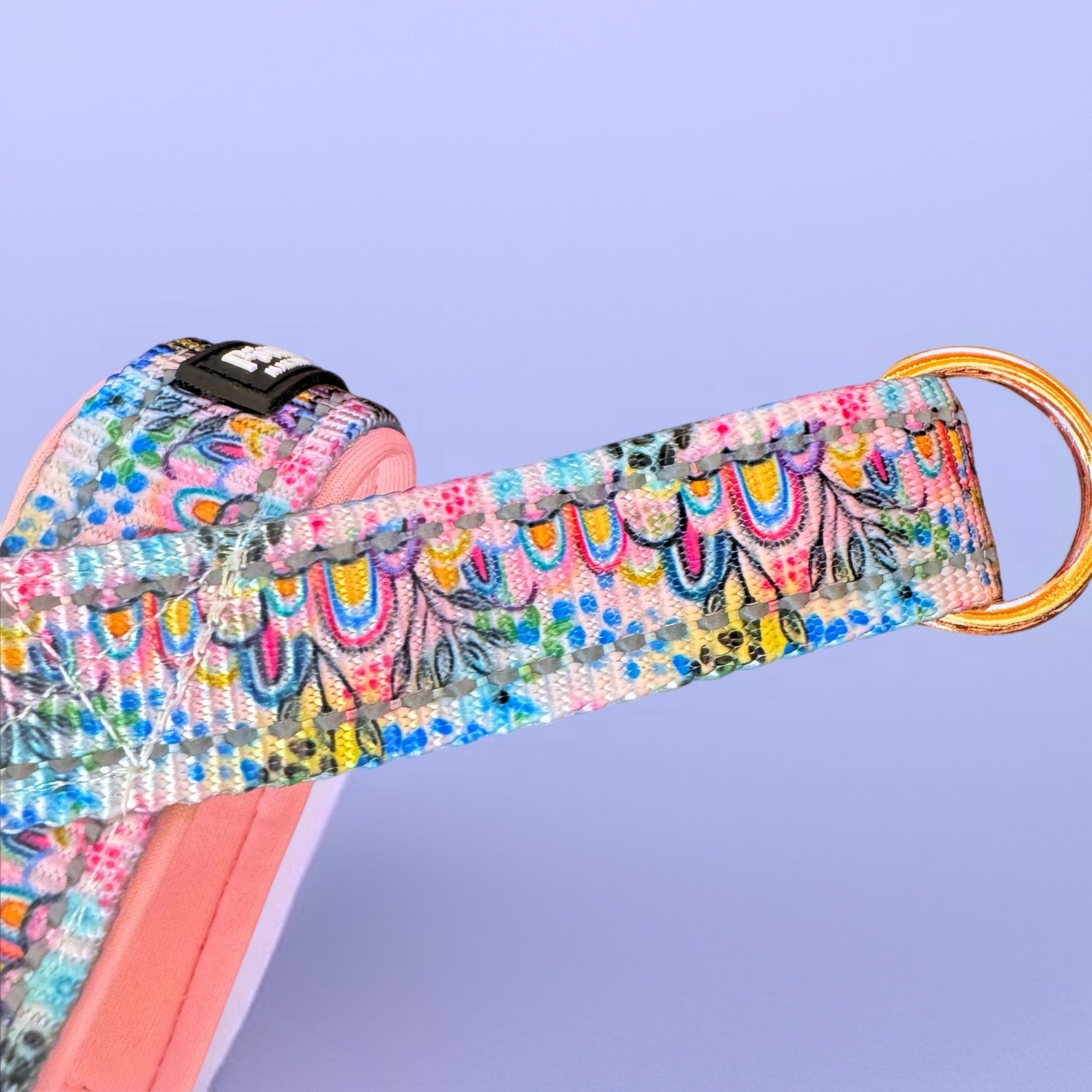 Colorful patterned dog harness with a rose gold clip on a light purple background